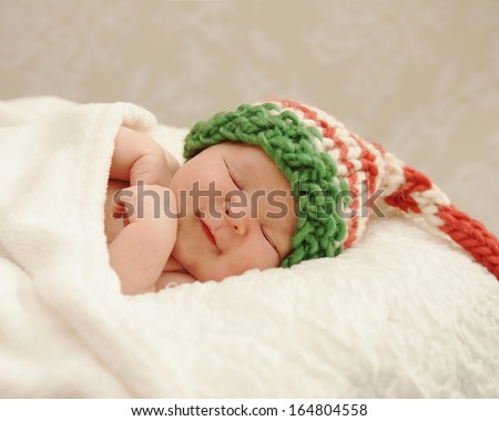 Healthy newborn baby smiling in sleep wearing a Christmas elf hat