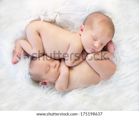 Sleeping Newborn Baby Twins, snuggled up together in womb like position  on white fur.