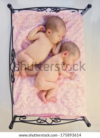 Tiny Sleeping Newborn Baby Twin Girls, cuddled up together in cute pose on wrought iron bed