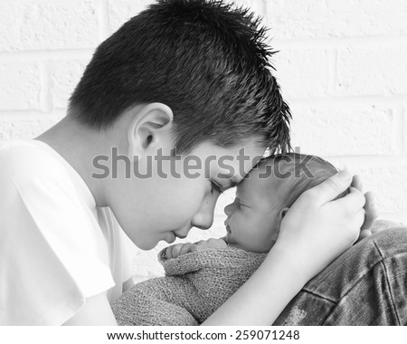 Newborn baby being held tenderly by big brother