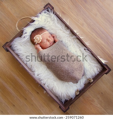 Newborn baby sleeping in vintage crate, wearing flower headband