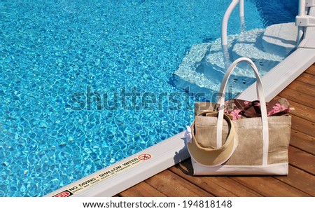 Beach bag with flip-flops and a sun visor sitting on a pool deck