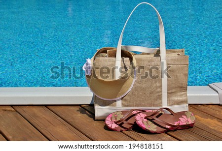 Beach bag with flip-flops and a sun visor sitting on a pool deck