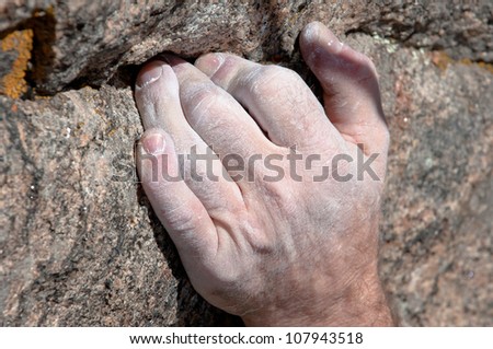 Hand of a rock climber is holding on to a small crack in the rock
