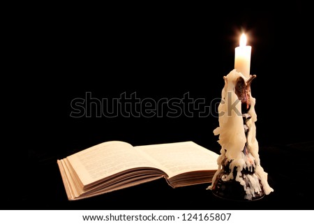 Old book and candle on dark background