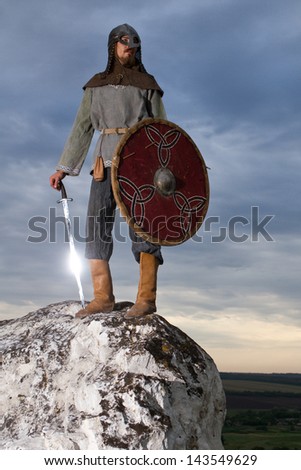 Knight  on a rock with a sword against blue cloudy sky