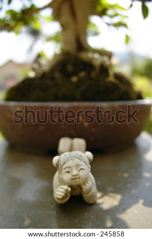 Statue of little Chinese girl in ancient costume, lying in front of a bonsai tree