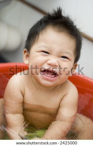Cute nine month old Asian baby boy having his bath in a bathtub