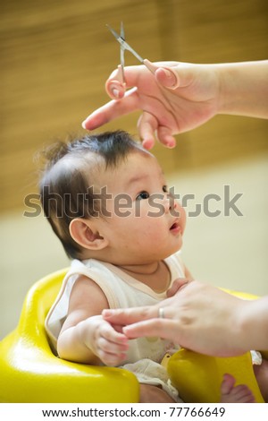 6 month old Asian baby girl having a haircut, while sitting in a yellow chair