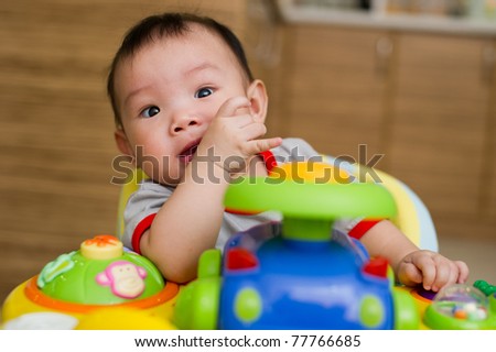 6 month old Asian baby girl chewing her fingers while sitting in a walker