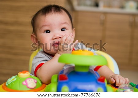 6 month old Asian baby girl chewing her fingers while sitting in a walker