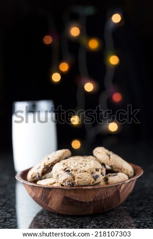 Chocolate chip cookies and milk on a granite table with lights on the background