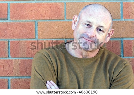 Portrait of a handsome middle aged man standing next to a brick wall with his hands folded