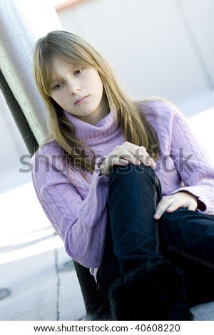 Young teenager girl with blond hair and bangs sitting with her knee bent in sad depressed expression