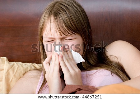 Sick with flu teenager girl in bed sneezing