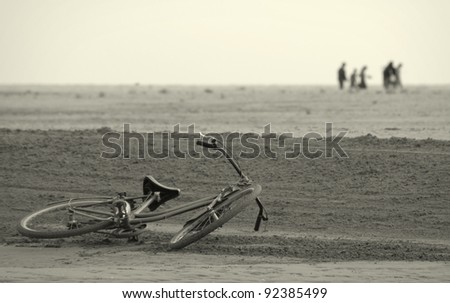 Abandoned bicycle along the beach and a group of defocused people walking far away