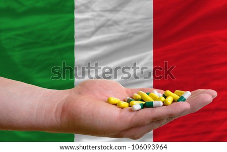 man holding capsules in front of complete wavy national flag of italy symbolizing health, medicine, cure, vitamines and healthy life