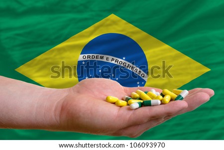 man holding capsules in front of complete wavy national flag of brazil symbolizing health, medicine, cure, vitamines and healthy life