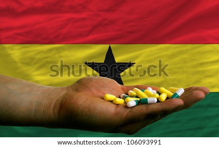 man holding capsules in front of complete wavy national flag of ghana symbolizing health, medicine, cure, vitamines and healthy life