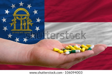 man holding capsules in front of complete wavy american state flag of georgia symbolizing health, medicine, cure, vitamines and healthy life