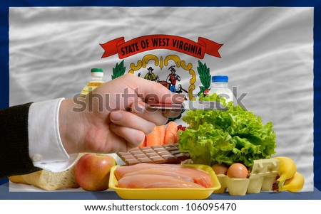 man stretching out credit card to buy food in front of complete wavy american state flag of west virginia