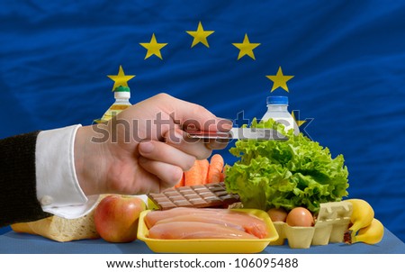 man stretching out credit card to buy food in front of complete wavy national flag of europe