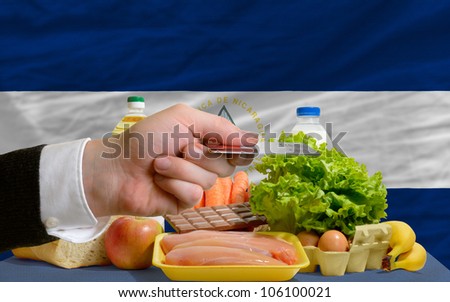 man stretching out credit card to buy food in front of complete wavy national flag of nicaragua