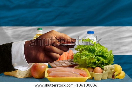 man stretching out credit card to buy food in front of complete wavy national flag of el salvador