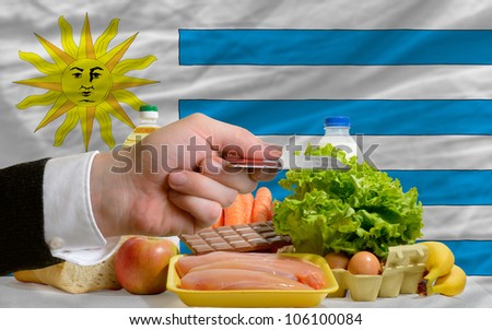 man stretching out credit card to buy food in front of complete wavy national flag of uruguay