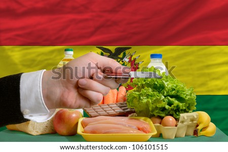 man stretching out credit card to buy food in front of complete wavy national flag of bolivia