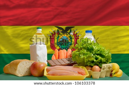complete national flag of bolivia covers whole frame, waved, crunched and very natural looking. In front plan are fundamental food ingredients for consumers, symbolizing consumerism an human needs