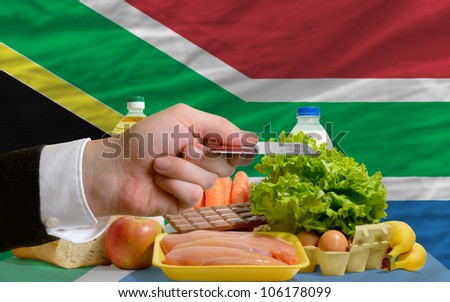 man stretching out credit card to buy food in front of complete wavy national flag of south africa