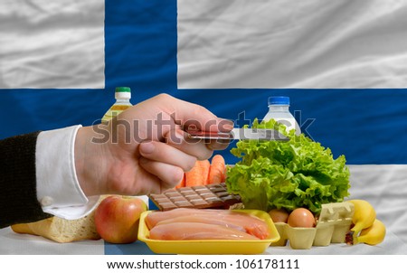 man stretching out credit card to buy food in front of complete wavy national flag of finland