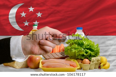 man stretching out credit card to buy food in front of complete wavy national flag of singapore