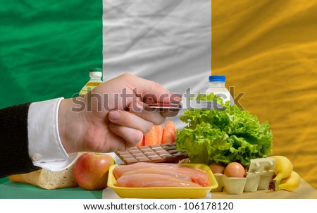 man stretching out credit card to buy food in front of complete wavy national flag of ireland