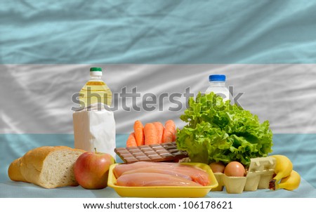 complete national flag of argentina covers whole frame, waved, crunched and very natural looking. In front plan are fundamental food ingredients for consumers, symbolizing consumerism