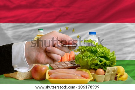 man stretching out credit card to buy food in front of complete wavy national flag of tajikistan