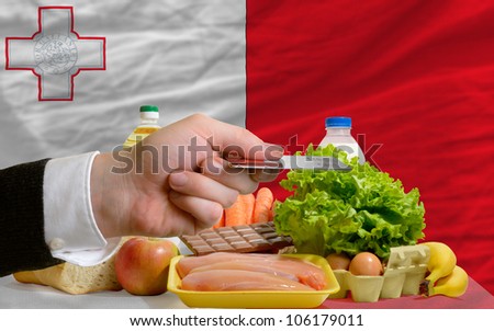 man stretching out credit card to buy food in front of complete wavy national flag of malta