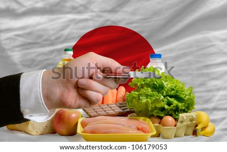 man stretching out credit card to buy food in front of complete wavy national flag of japan