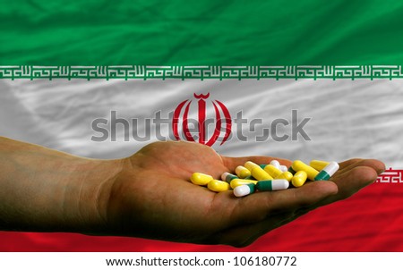 man holding capsules in front of complete wavy national flag of iran symbolizing health, medicine, cure, vitamins and healthy life