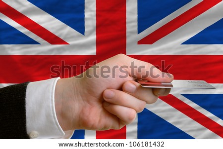 man stretching out credit card to buy goods in front of complete wavy national flag of great britain