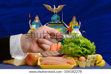man stretching out credit card to buy food in front of complete wavy american state flag of new york