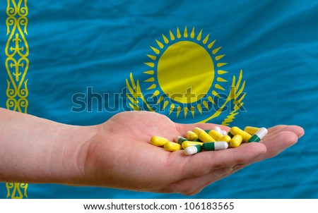 man holding capsules in front of complete wavy national flag of kazakhstan symbolizing health, medicine, cure, vitamins and healthy life