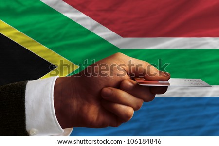 man stretching out credit card to buy goods in front of complete wavy national flag of south africa