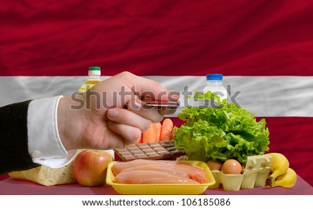 man stretching out credit card to buy food in front of complete wavy national flag of latvia