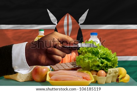 man stretching out credit card to buy food in front of complete wavy national flag of kenya
