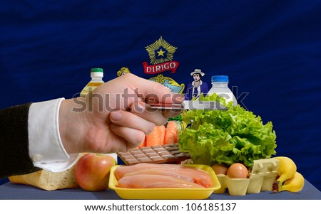 man stretching out credit card to buy food in front of complete wavy american state flag of maine