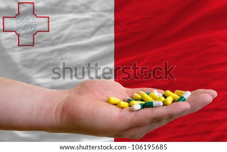 man holding capsules in front of complete wavy national flag of malta symbolizing health, medicine, cure, vitamins and healthy life