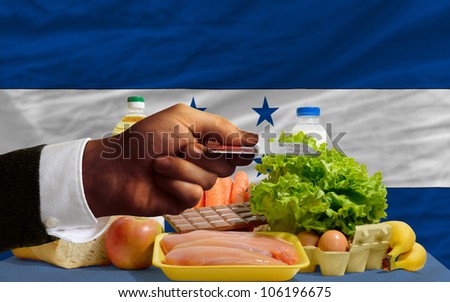man stretching out credit card to buy food in front of complete wavy national flag of honduras