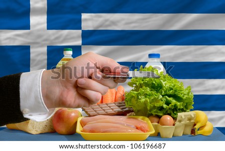 man stretching out credit card to buy food in front of complete wavy national flag of greece